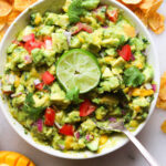 A white bowl filled with mango guacamole, garnished with lime and cilantro.