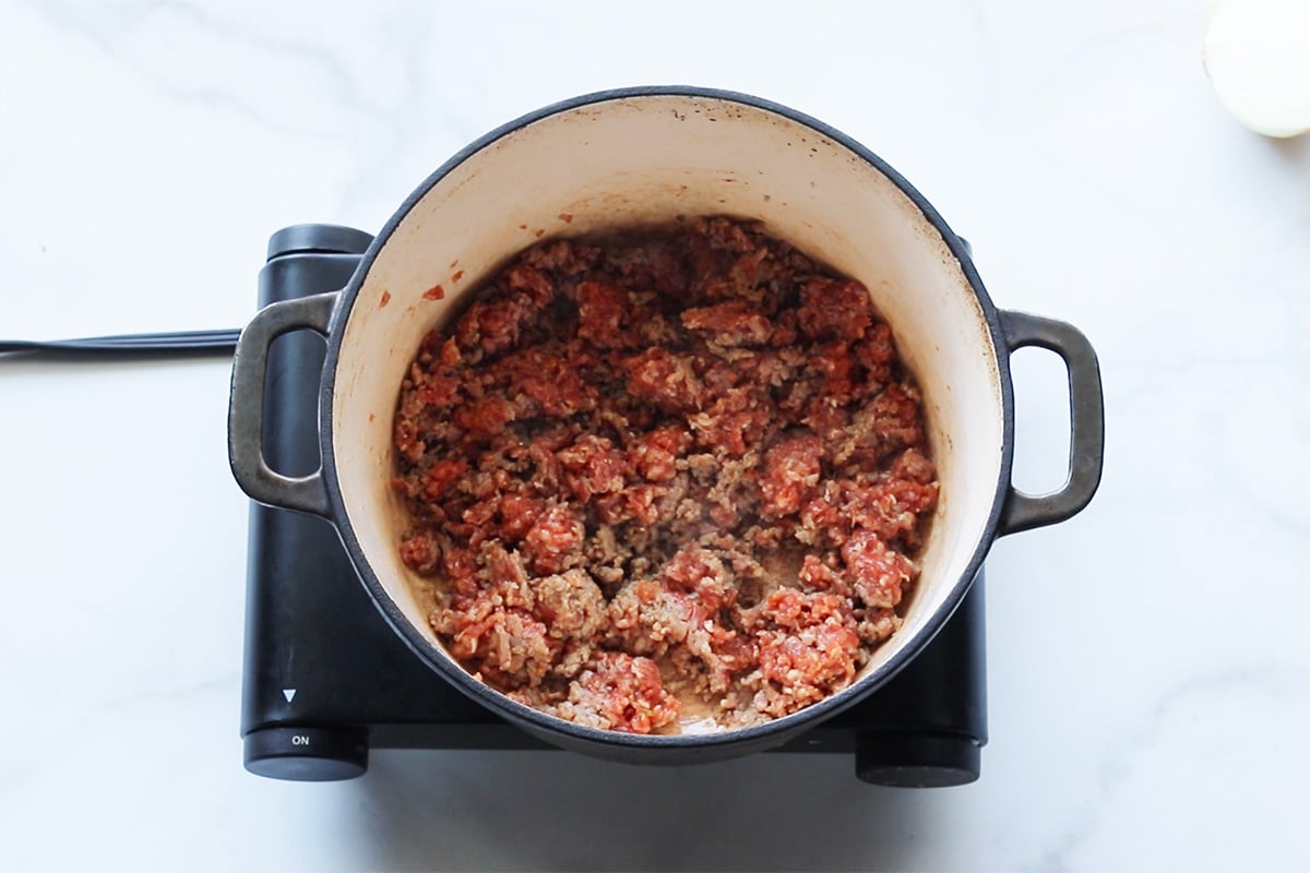 Overhead view of ground Italian sausage cooking in a large soup pot.