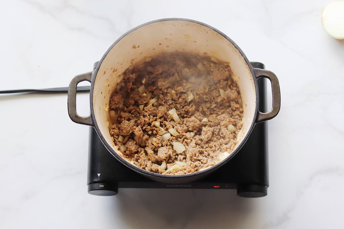 Overhead view of cooked ground meat and sauteed diced onions in a large Dutch oven.