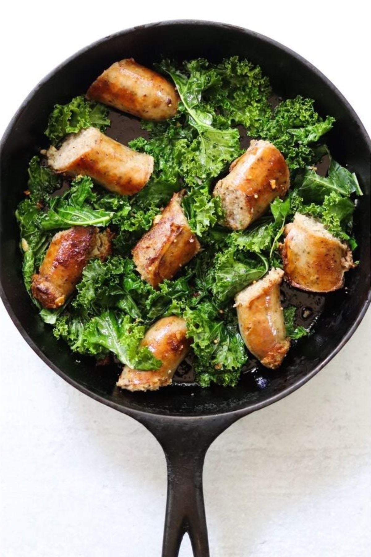 Sliced sausage and fresh kale cooking in a black cast iron skillet.