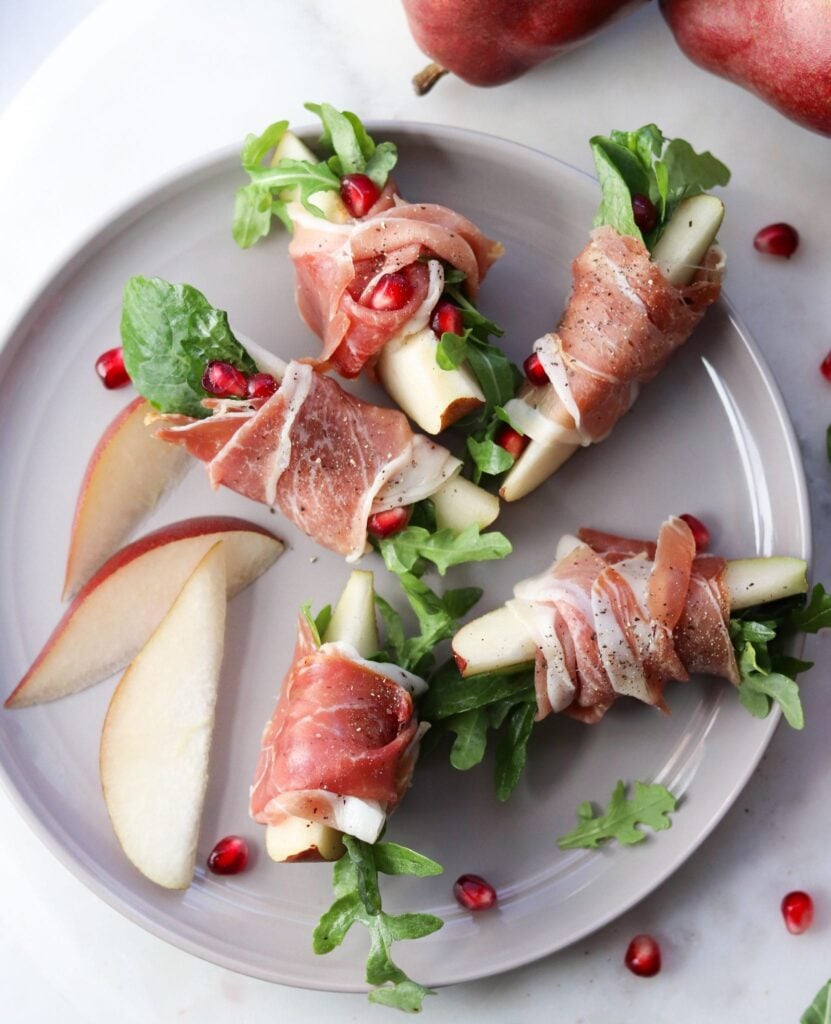 A small gray plate with slices of pear wrapped in prosciutto with a few leaves of arugula tucked inside. Finished Dish