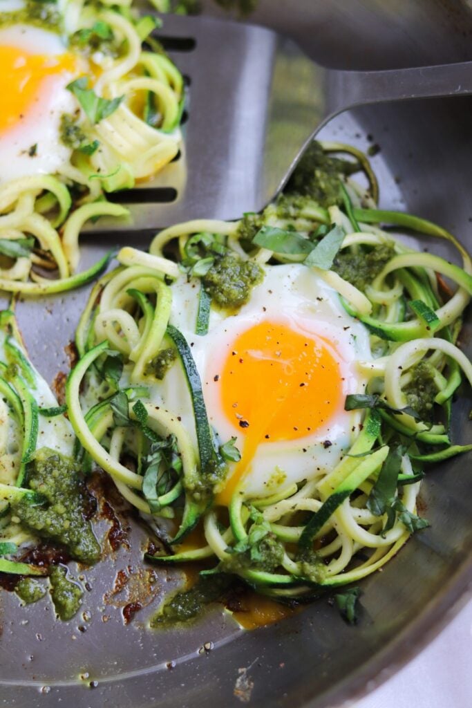 Close up of low carb pesto and spiralized zucchini egg nests in a skillet.