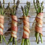 Close up of cooked Bacon Wrapped Asparagus on a metal rack.