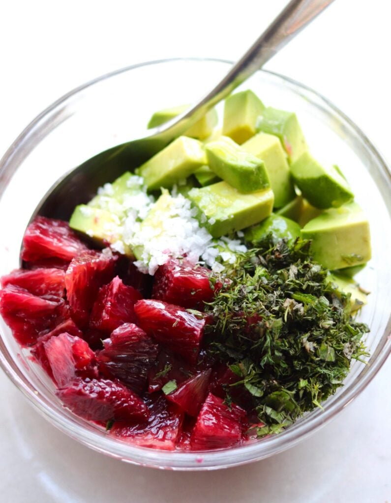 A small bowl filled with diced avocado, segmented oranges, herbs and salt.