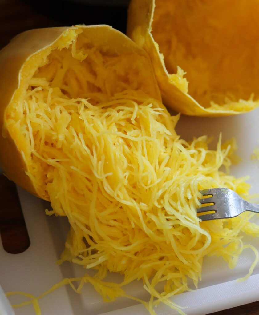 A fork pulling strands of tender spaghetti squash from inside of the peel.
