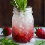 Mason jar filled with crushed ice, smashed strawberries and fresh basil garnished with fresh basil leaves and a reusable straw.