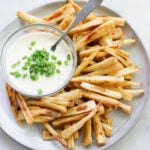 Crispy roasted parsnip fries on a gray plate with dipping sauce.