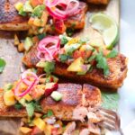 Salmon fillets on a cutting board, topped with peach salsa.