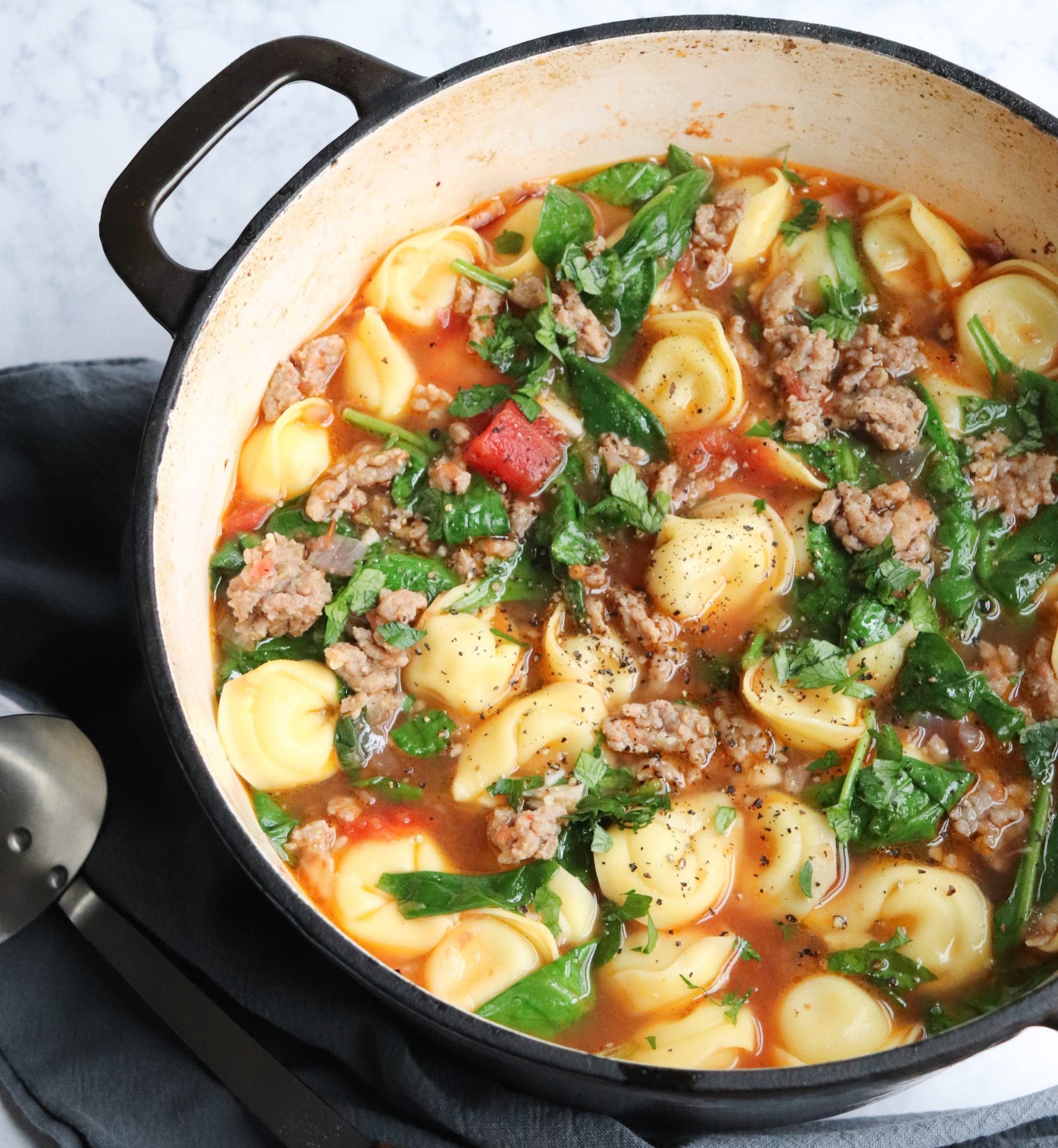 Soup with sausage, tortellini, and spinach in a stock pot.