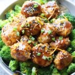 A bowl of paleo chicken meatballs garnished with sesame seeds and green onions, served with broccoli.