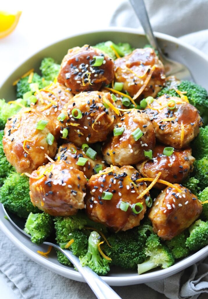 A close up shot of the Asian Orange Chicken Meatballs, served in a gray dish over steamed broccoli.