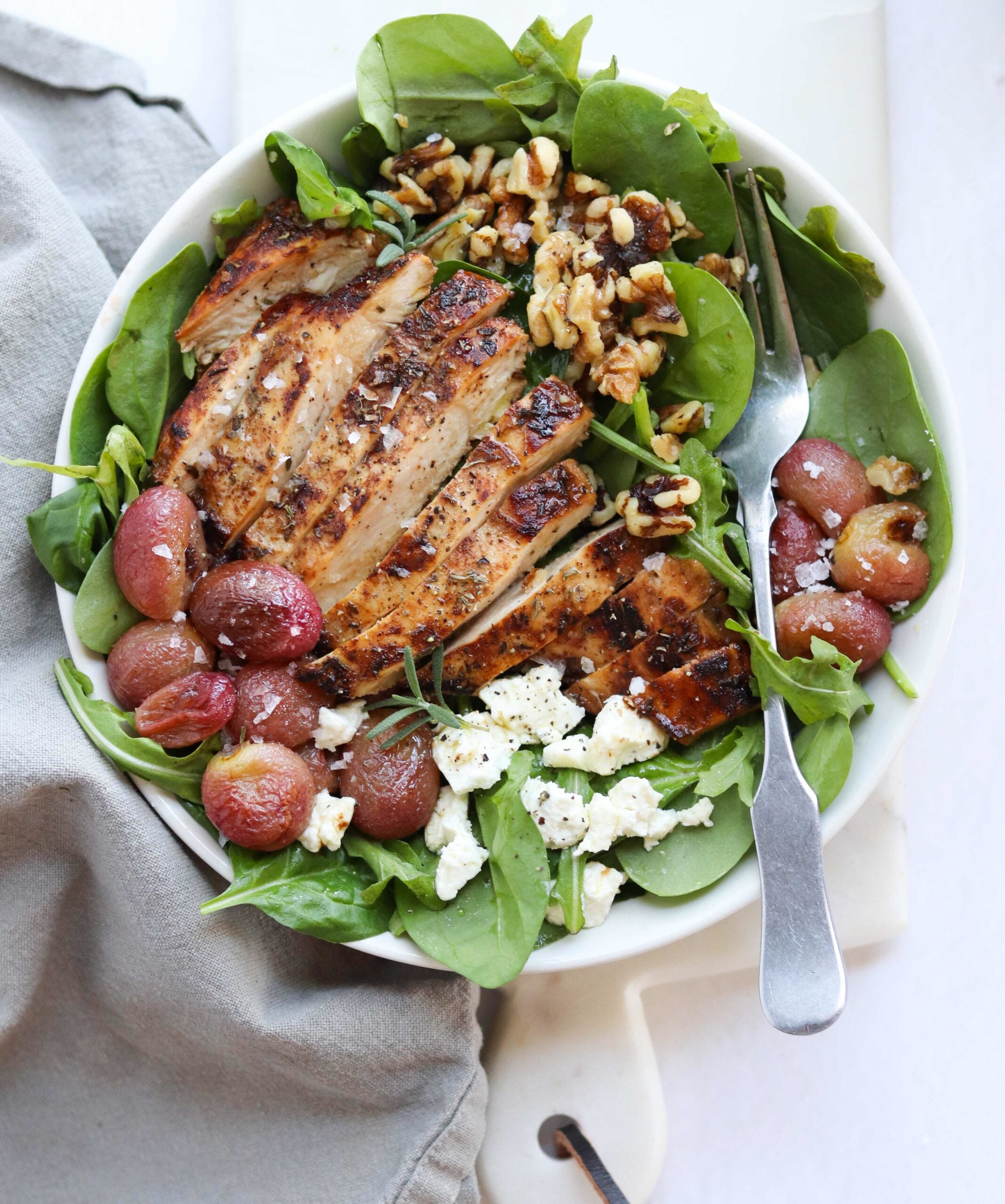 Mediterranean chicken salad consisting of pan seared chicken, roasted grapes, crumbled cheese and chopped walnuts served over baby spinach.