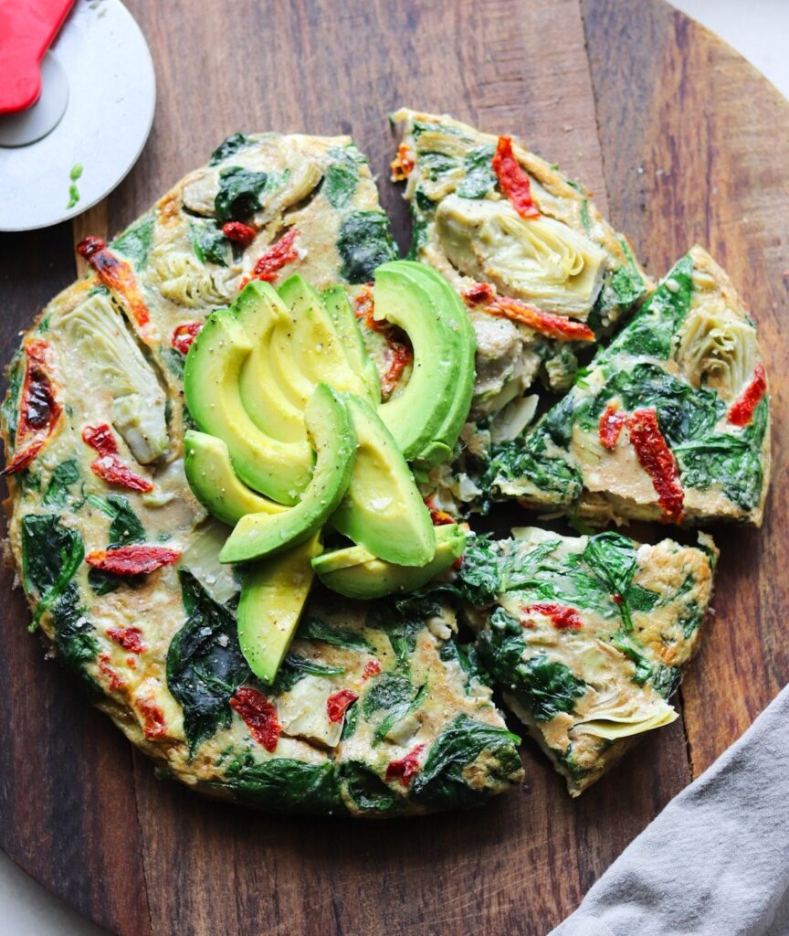 The finished frittata on a dark wooden cutting board, cut into slices and served with avocado.