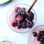 Two glasses filled with avocado and mixed fruit smoothie and topped with frozen berries.