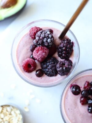 Two glasses filled with avocado and mixed fruit smoothie and topped with frozen berries.