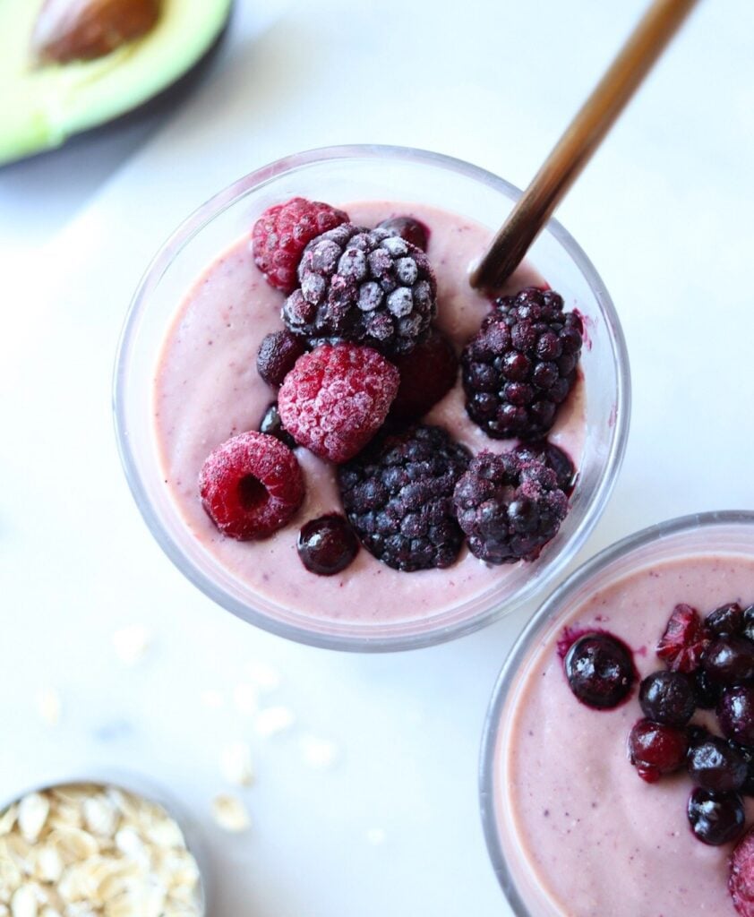 Two glasses filled with avocado and mixed fruit smoothie and topped with frozen berries.