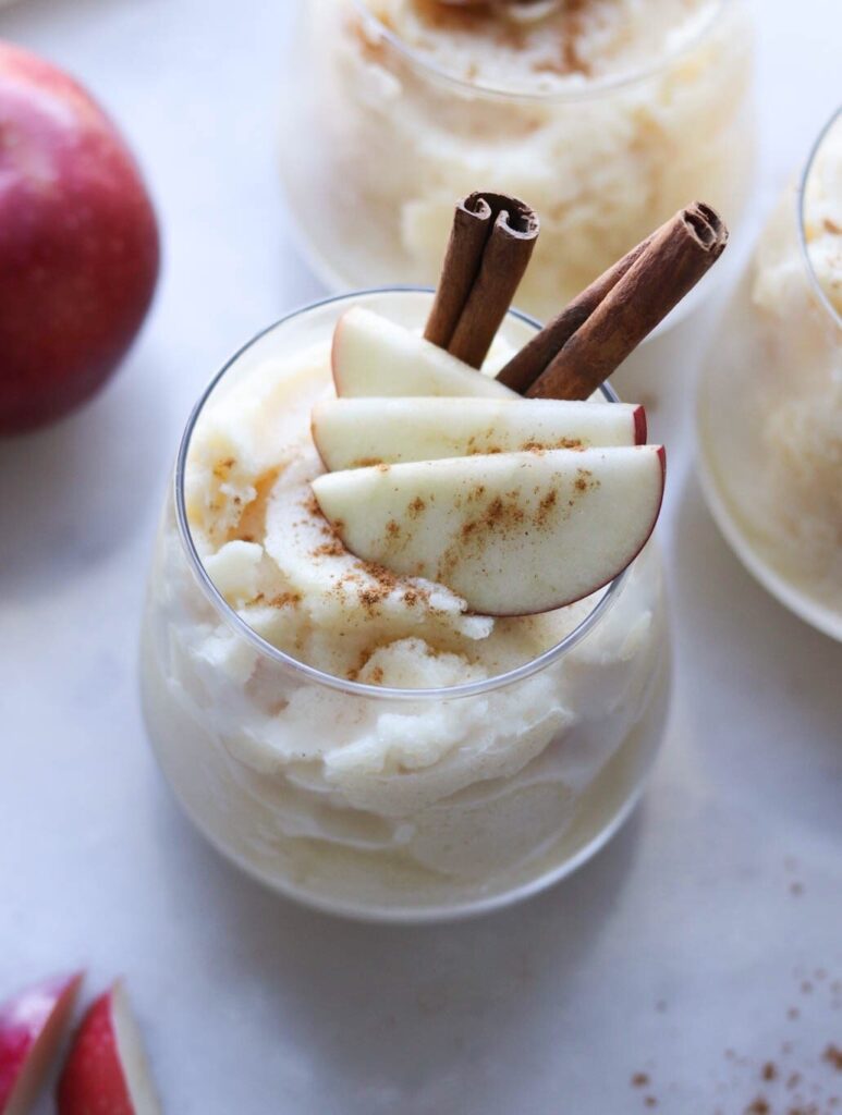 Frozen Bourbon Apple Cider Cocktail slushie presented in a small glass, garnished with cinnamon sticks and apple slices.