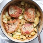 Pork Chops, Sauerkraut, apple and potatoes cooked in a dutch oven on a white marble board with large serving spoon.