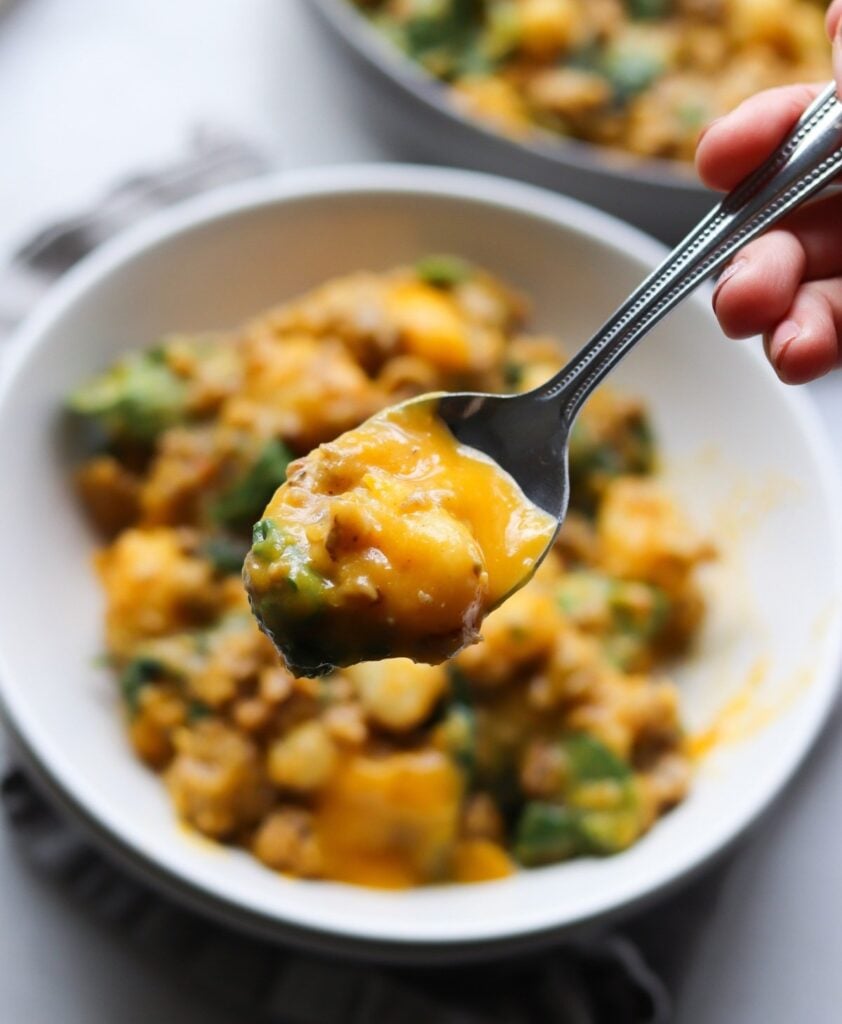 A spoon held in one hand over the bowl with one bite of the finished sausage and power greens skillet.