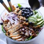 The Grilled Chicken Salad plated in a large glass bowl with the lemon dijon salad dressing being drizzled on top.