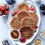 Paleo Waffles laid out on a white serving dish, surrounded by small dishes with all the toppings.