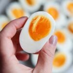 Close up of a hand holding one half of a jammy boiled egg.