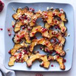 Roasted Acorn Squash on a blue serving platter, drizzled with maple tahini dressing and sprinkled with pomegranate and crushed walnuts.