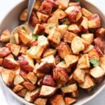 A gray bowl with crispy air fryer red potatoes and a large serving spoon.