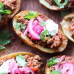Close up top view of chili stuffed potato skins topped with pickled onions, sour cream, and cilantro.