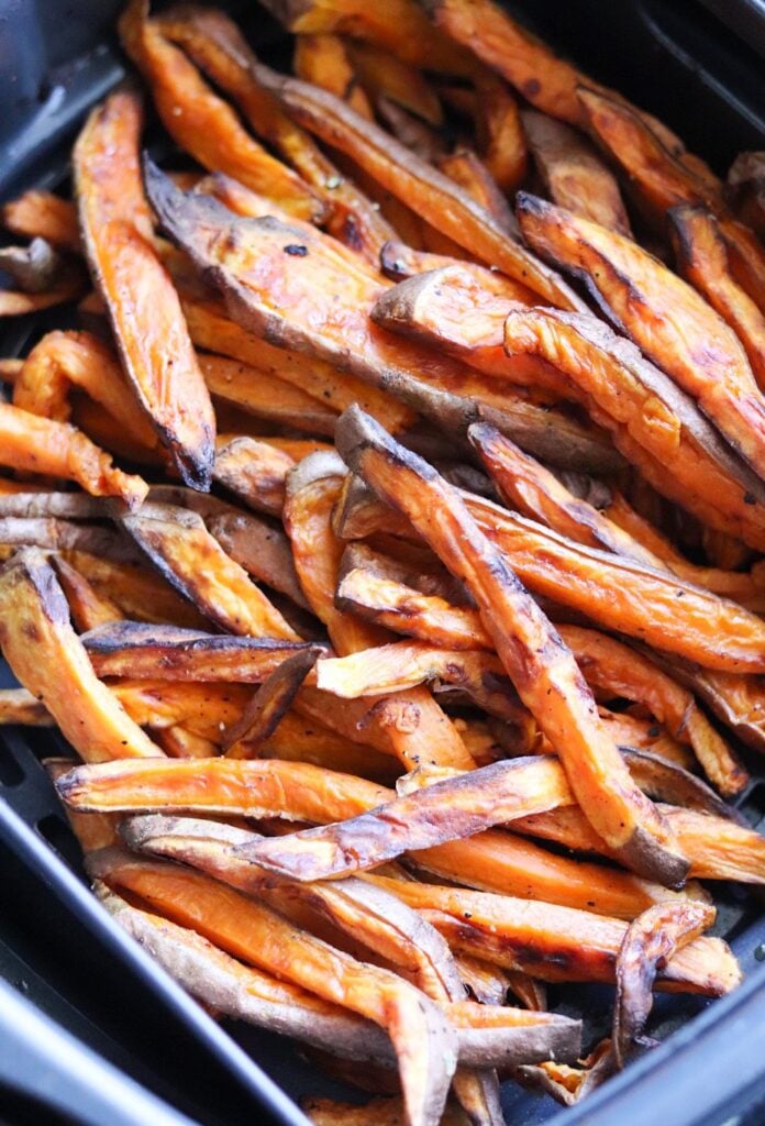 A pile of crispy air fried sweet potato Fries with skin, displayed in a black container.