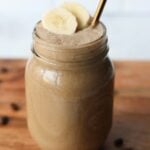 A mason jar filled with Banana Coffee smoothie on a wooden cutting board.