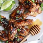 Honey Sriracha Chicken Wings sprinkled with sesame seeds and onions on a white plate.