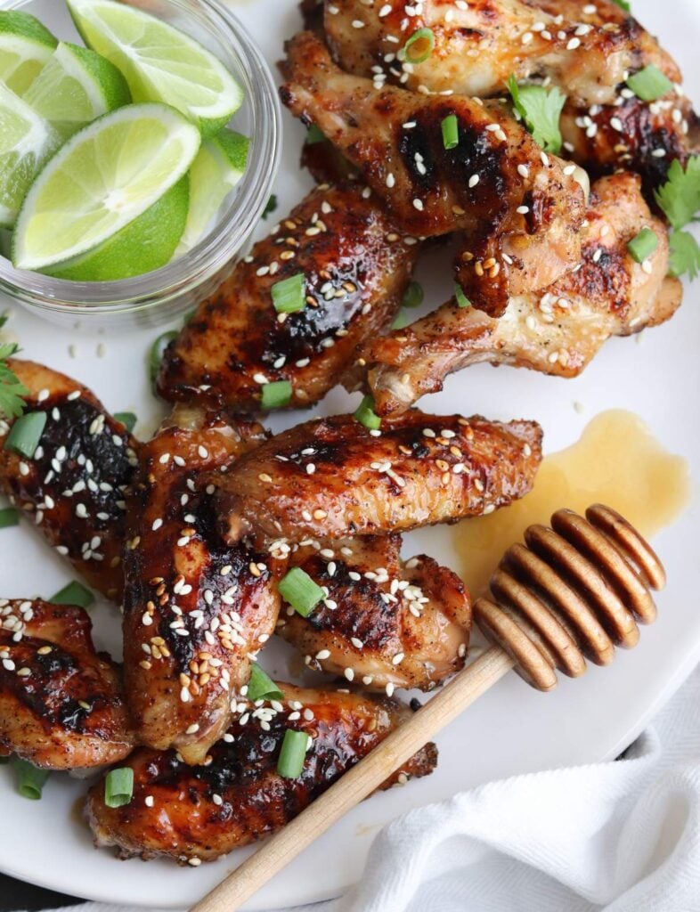 Honey Sriracha Chicken Wings sprinkled with sesame seeds and onions on a white plate.