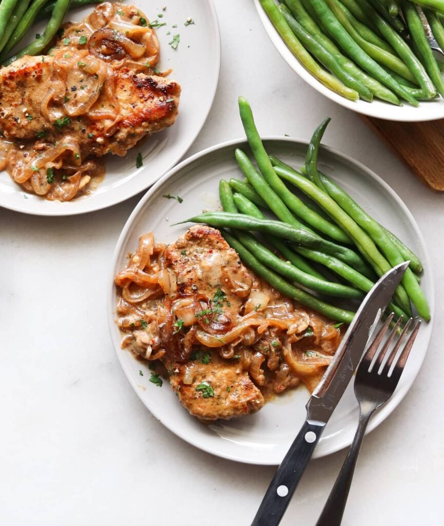 Cook pork chop on a gray plate, serve with green beans.