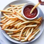 A gray plate with crispy French fries and a small ramekin of ketchup.