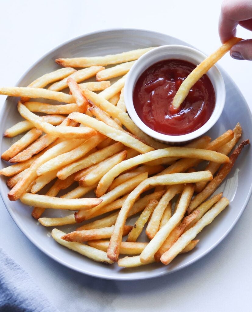 A gray plate with crispy French fries and a small ramekin of ketchup.