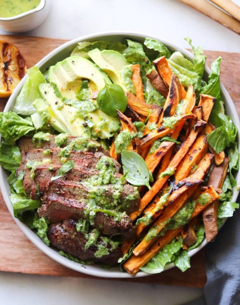 Avocado Green Goddess Dressing drizzled on a salad with steak and sweet potato fries