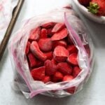 Close up top down of a large plastic bag filled with frozen strawberries.