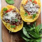 Two keto spaghetti squash stuffed with ground beef and basil on a cutting board.