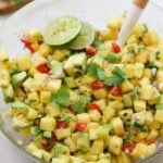A glass boowl filled with pineapple avocado salsa, garnished with lime.