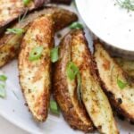 Close up of cooked crispy potato wedges beside a small dish of ranch.