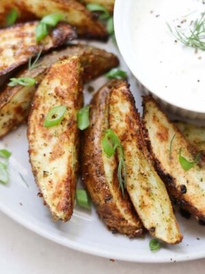 Close up of cooked crispy potato wedges beside a small dish of ranch.