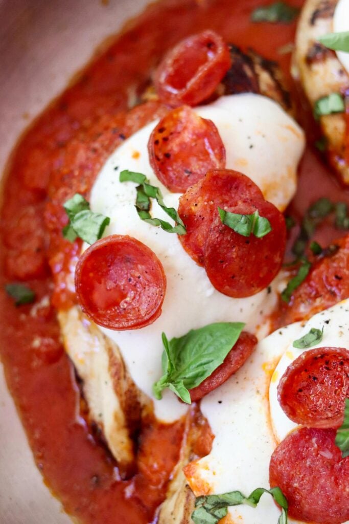 Close up of one finished piece of pizza chicken in the skillet garnished with sliced basil.