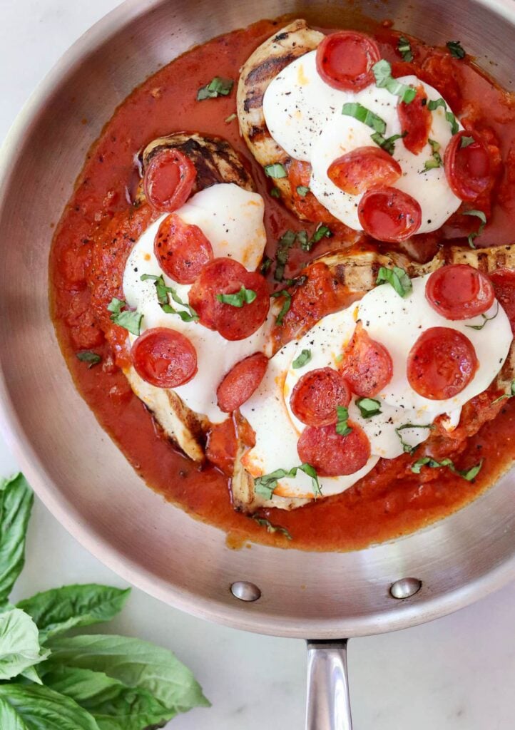 Pizza chicken in a skillet: three grilled chicken breasts in tomato sauce, topped with melted mozzarella, pepperoni slices, and fresh basil.