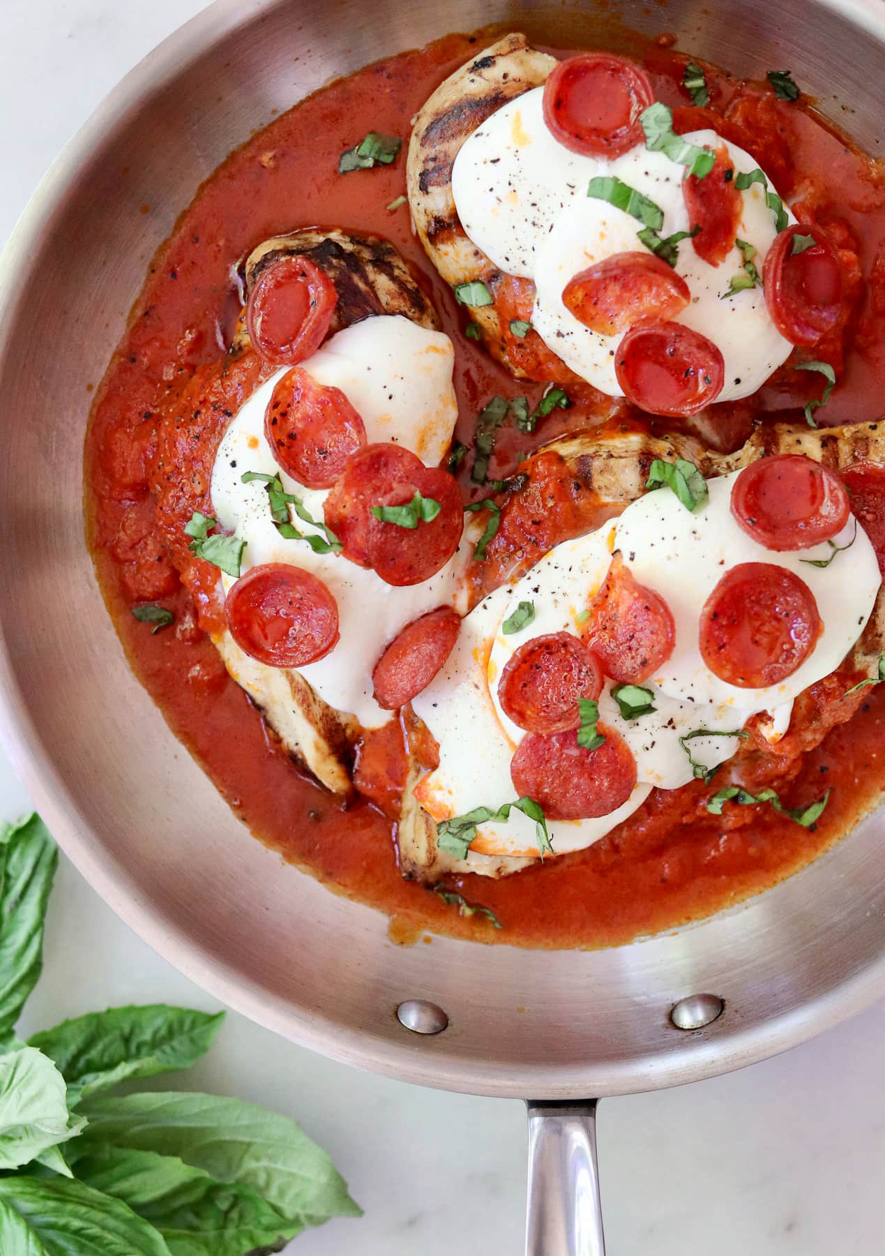 Tender pizza chicken: three grilled chicken breasts in tomato sauce, topped with melted mozzarella, pepperoni slices, and fresh basil—bringing keto pizza flavors to your skillet.