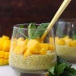 Side view of a small glass filled with mango chia pudding, topped with diced mango and mint leaves.