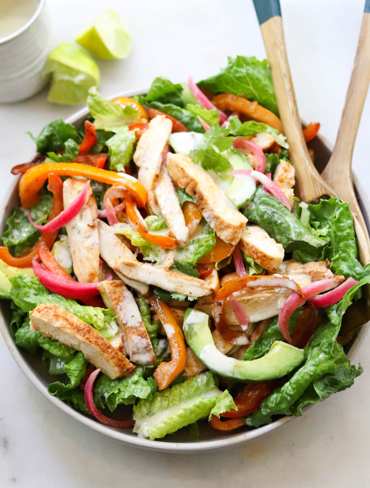 The finished spicy chicken fajita salad tossed together in a large bowl with wooden serving spoons. 