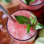 Close up top down of a tall glass filled with ice and watermelon-lime juice, garnished with fresh mint.