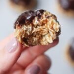 Side view close up of a hand holding one almond butter energy ball with a bite taken out.