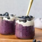 Side view close up of a small jar filled with blueberry chia pudding, topped with yogurt and fresh blueberries.
